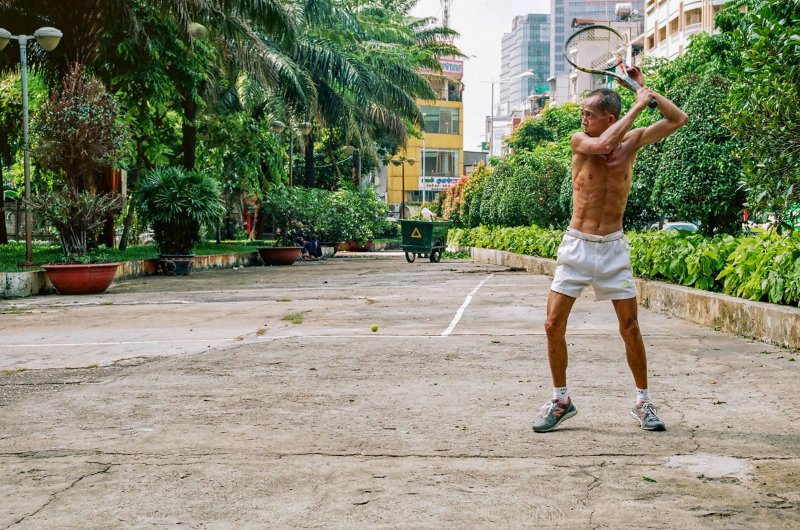 Mann hält zum Schlag einen Tennisschläger draußen über seinem Kopf