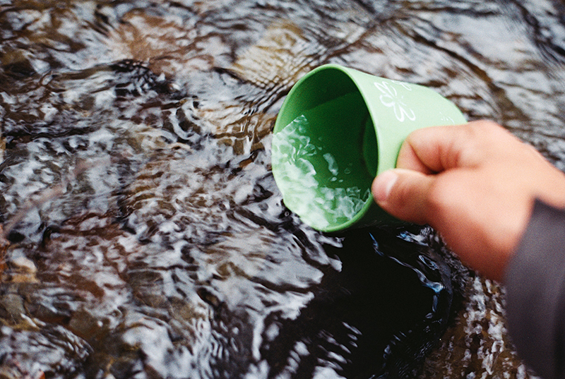 Ein Trinkbecher wird mit Wasser aus einem See aufgefüllt