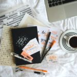 Handlettering Buch & Stifte auf Bettdecke mit Kaffe und Laptop