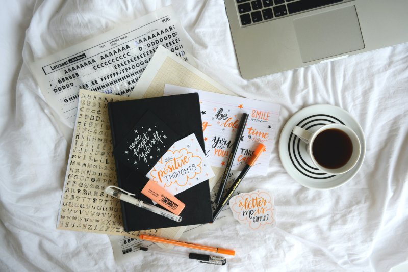 Handlettering Buch & Stifte auf Bettdecke mit Kaffe und Laptop