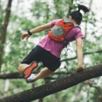 Trailrunner mit Rucksack springt über Baumstamm