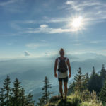 Wanderer mit Trinkrucksack auf einem Berg mit Landschaft im Hintergrund