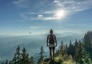 Wanderer mit Trinkrucksack auf einem Berg mit Landschaft im Hintergrund