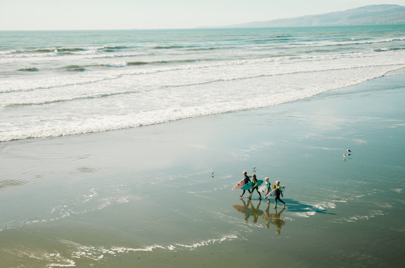 Kinder laufen am Strand mit Surfbrett im Neoprenanzug