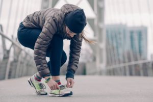 Frau bindet sich nach dem Laufen gehen die Schuhe im Winter.