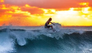 Surfer mit Surfer-Sonnenbrilleauf einer Welle mit Sonnenuntergang im Hintergrund