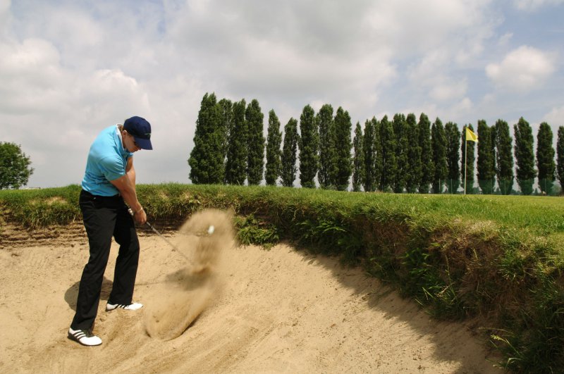 Golfball wird mit dem Golfschläger aus dem Sand geschlagen