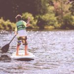 Ein Junge steht auf einem SUP und trägt eine Schwimmweste.