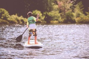 Ein Junge steht auf einem SUP und trägt eine Schwimmweste.