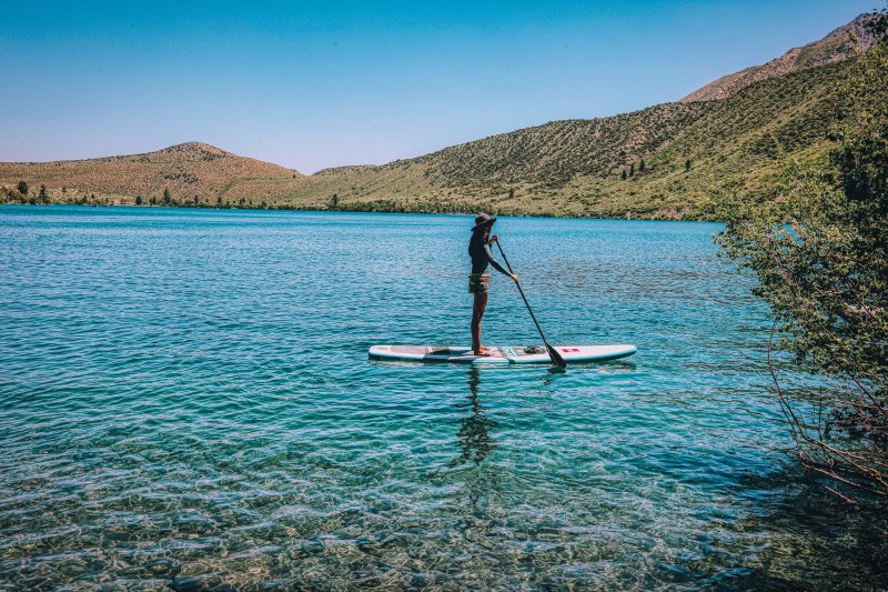 Eine weibliche Person steht auf einem Kinder SUP-Board und paddelt.