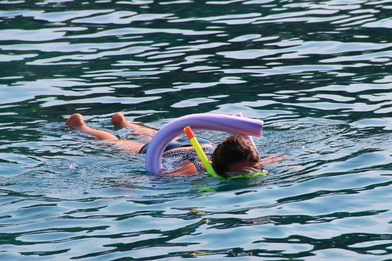 Kind schwimmt mit Poolnudel in Wasser