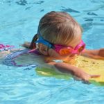 Mädchen lernt Schwimmen mit einem Schwimmbrett im Wasser.