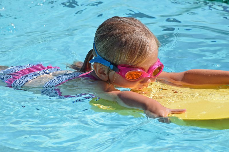 Mädchen lernt Schwimmen mit einem Schwimmbrett im Wasser.