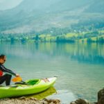 Kanufahrer sitzt in Paddelhosen am See.