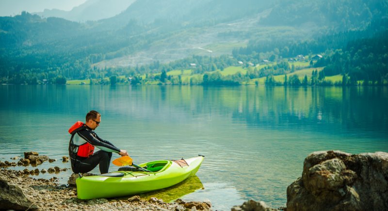 Kanufahrer sitzt in Paddelhosen am See.