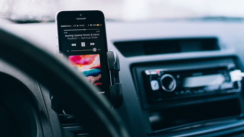 Smartphone mit laufendem Musikplayer in einem Auto neben dem Lenkrad befestigt und mit einem Autoradio im Hintergrund