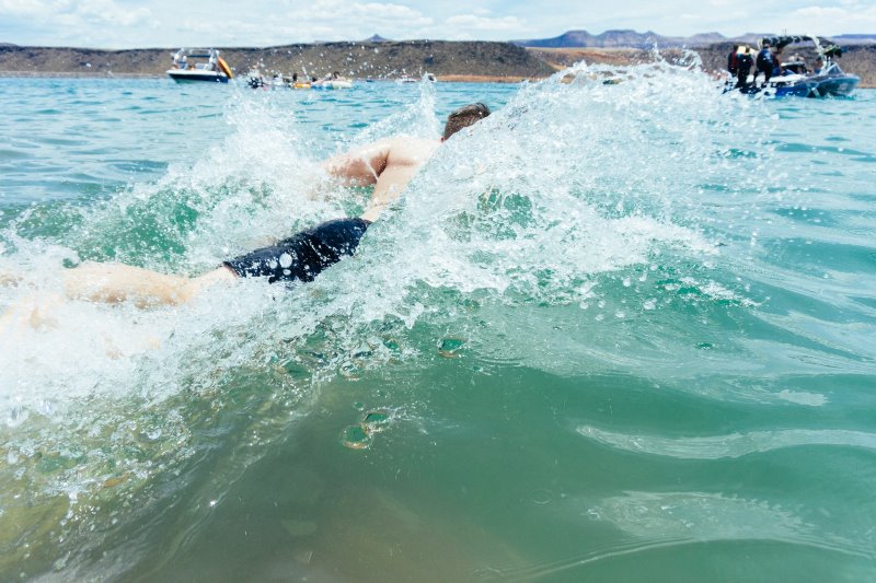 Mann schwimmt energisch im Wasser vom Schlauchboot aus