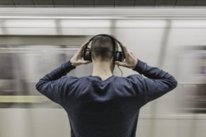 Ein Mann setzt sich Kopfhörer auf, während eine U-Bahn vorbei fährt.