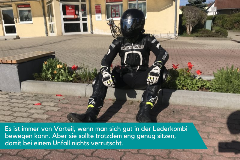 Eine Person sitzt mit der Lederkombi auf einem Bürgersteig