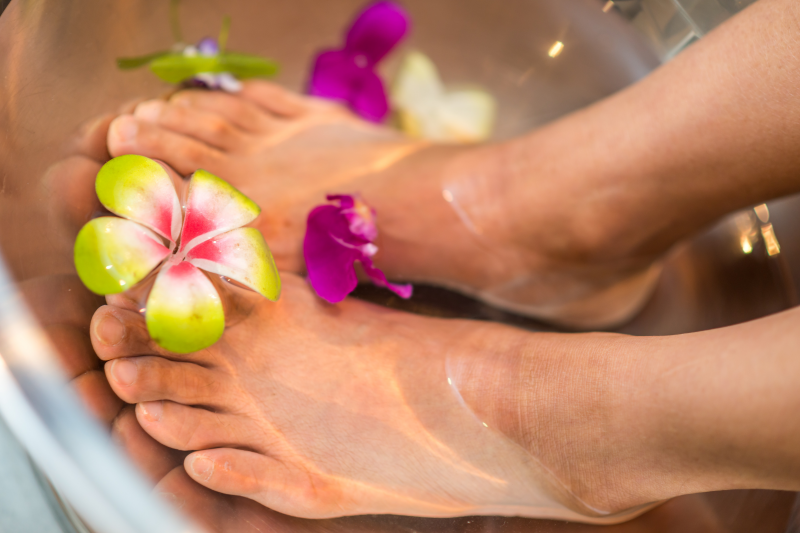 Frau nimmt Fußbad mit Blumen im Wasser