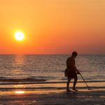 Mann mit Metalldetektor am Strand im Sonnenuntergang