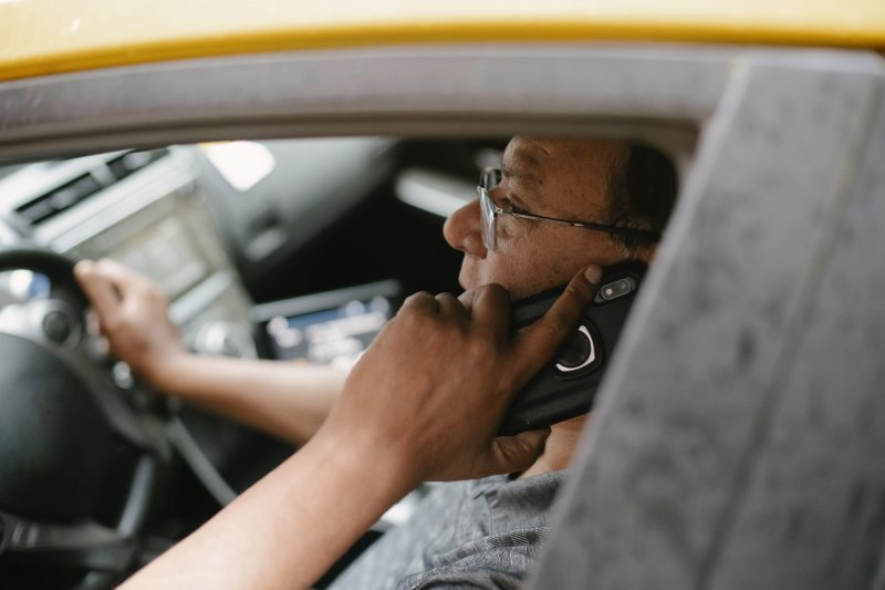 Mann telefoniert gefährlicherweise mit seinem Smartphone beim Fahren im Auto.