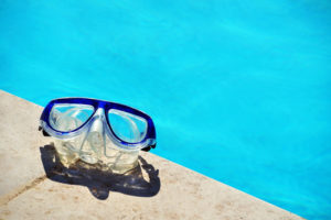 Eine Taucherbrille liegt auf einem Schwimmbeckenrand. Im Hintergrund sieht man blaues Wasser.