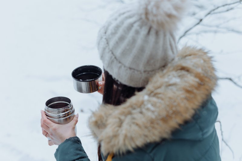 Frau ist im Schnee und trinkt aus ihrer Thermoskanne