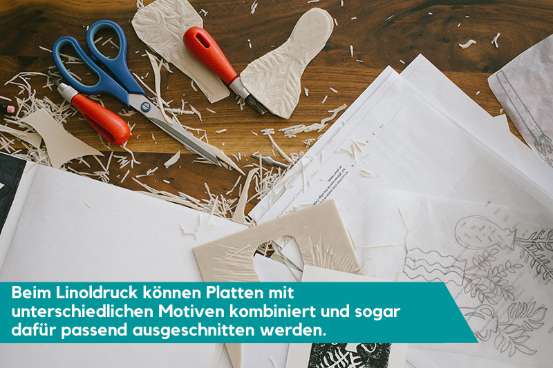 Auf einem Tisch liegt eine Auswahl an Materialien, die für einen Linoldruck verwendet werden können: Papiere, Schere, Linolschnittbesteck und so weiter. Die Beschriftung liest: "Beim Linoldruck können Platten mit unterschiedlichen Motiven kombiniert und sogar dafür passend ausgeschnitten werden."