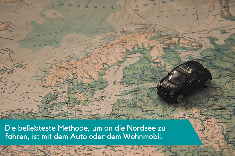 Ein kleines Spielzeugauto, platziert auf einer Karte, die den nördlichen Teil Deutschlands und Finnland zeigt. Die Beschriftung lautet: Die beliebteste Methode, um an die Nordsee zu fahren, ist mit dem Auto oder dem Wohnmobil. 