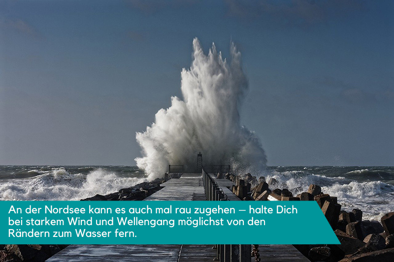 Eine massive Welle, die an der Nordsee auf einen Deich prallt - ein wahres Naturschauspiel. Die Beschriftung lautet: An der Nordsee kann es auch mal rau zugehen - halte Dich bei starkem Wind und Wellengang möglichst von den Rändern zum Wasser fern.