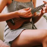 eine sitzende Frau spielt Ukulele auf einem Stuhl