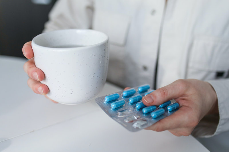 Frau hält Tabletten und ein Becher Wasser in der Hand