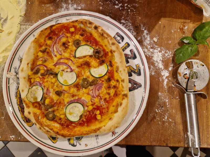 Fertige Gemüse-Pizza mit Zucchini, Mais und roten Zwiebeln.