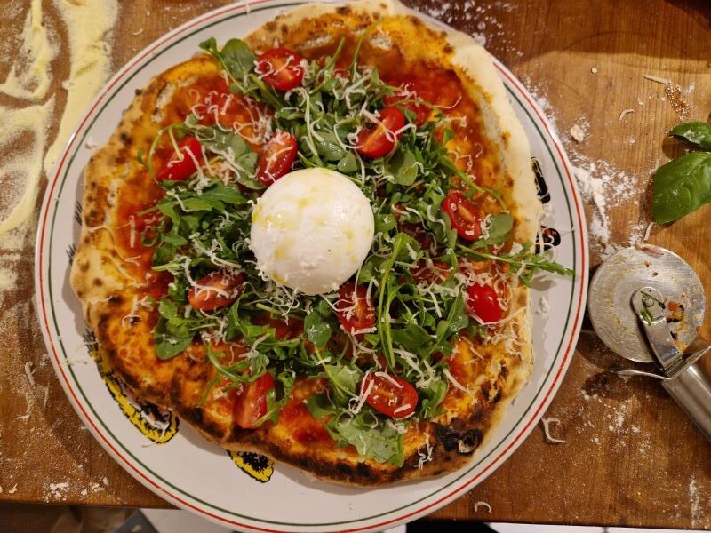 Pizza mit Rucola, Tomaten und Burrata-Käse.