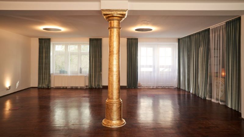 Ein eleganter, leerer Yoga-Raum mit einer goldenen Säule in der Mitte, großen Fenstern und sanfter Beleuchtung.