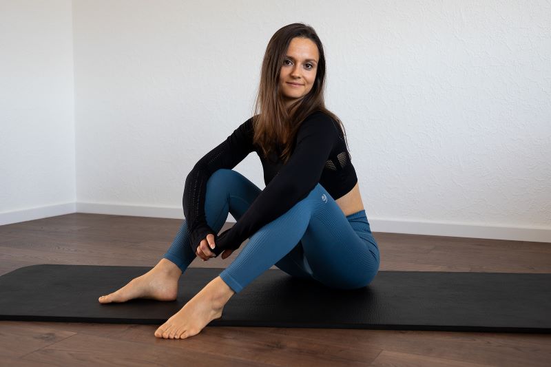 Eine Yogalehrerin sitzt entspannt auf einer Yogamatte und schaut lächelnd in die Kamera.