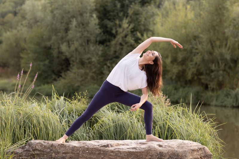 Eine Frau macht draußen auf einem Felsen eine Yoga-Pose in der Natur.