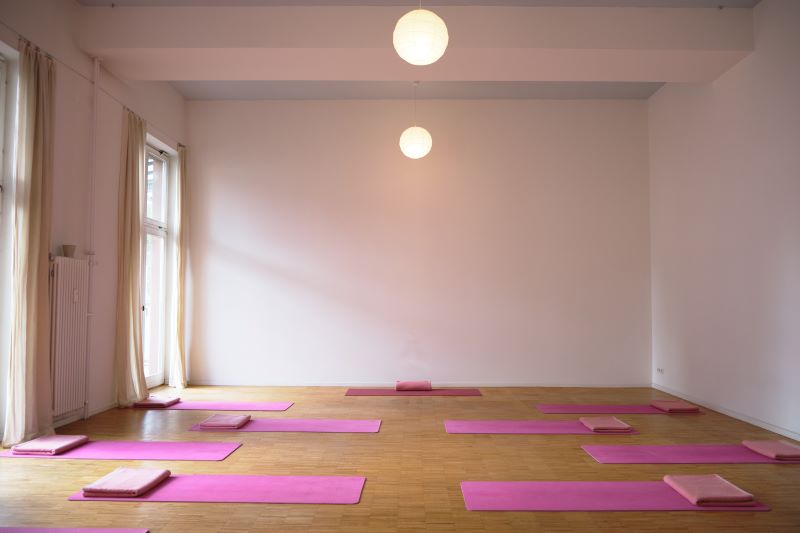 Ein ruhiger und heller Yogaraum mit rosafarbenen Matten und Kissen, bereit für die nächste Yogastunde.